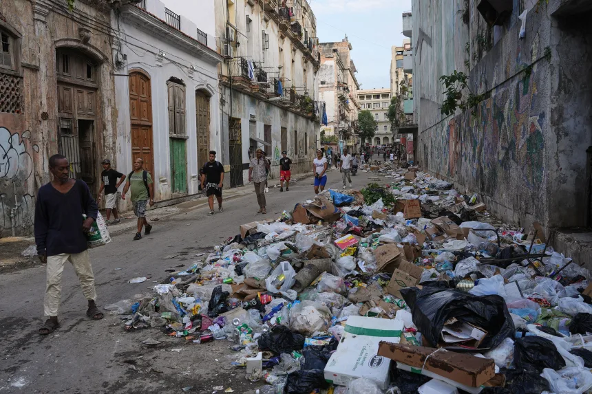 People walk next to trash on a street in Havana